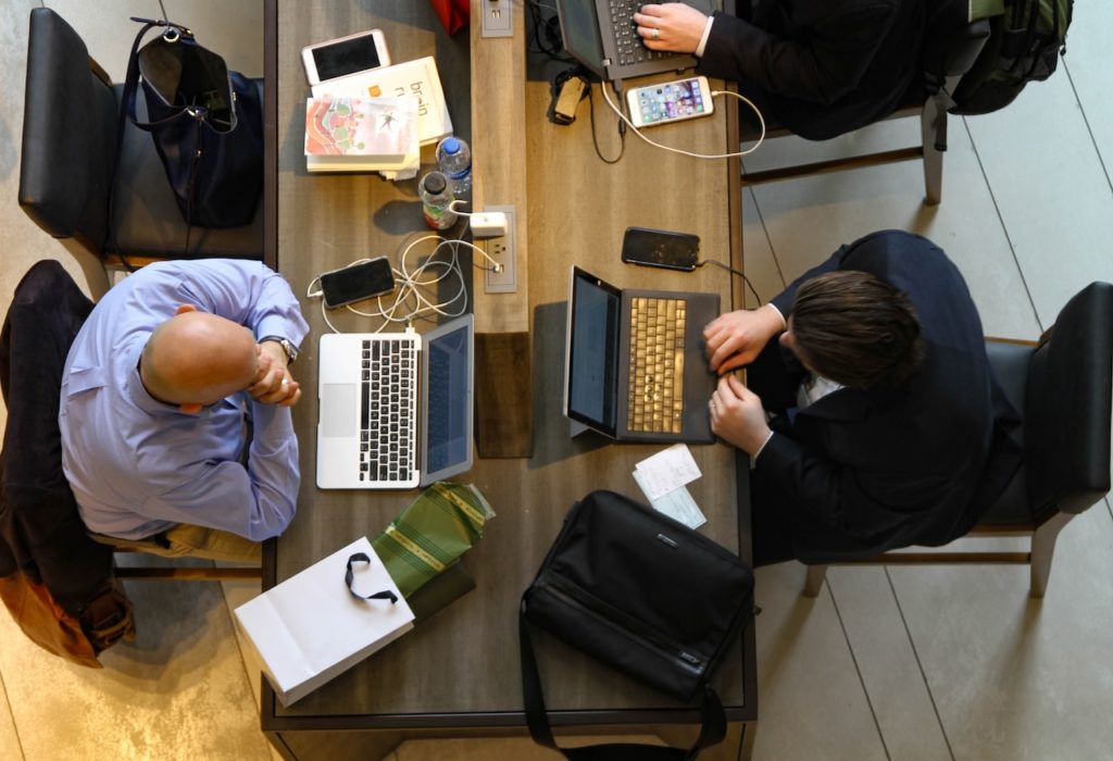 two men sit across from each other with a Mac laptop and a PC laptop